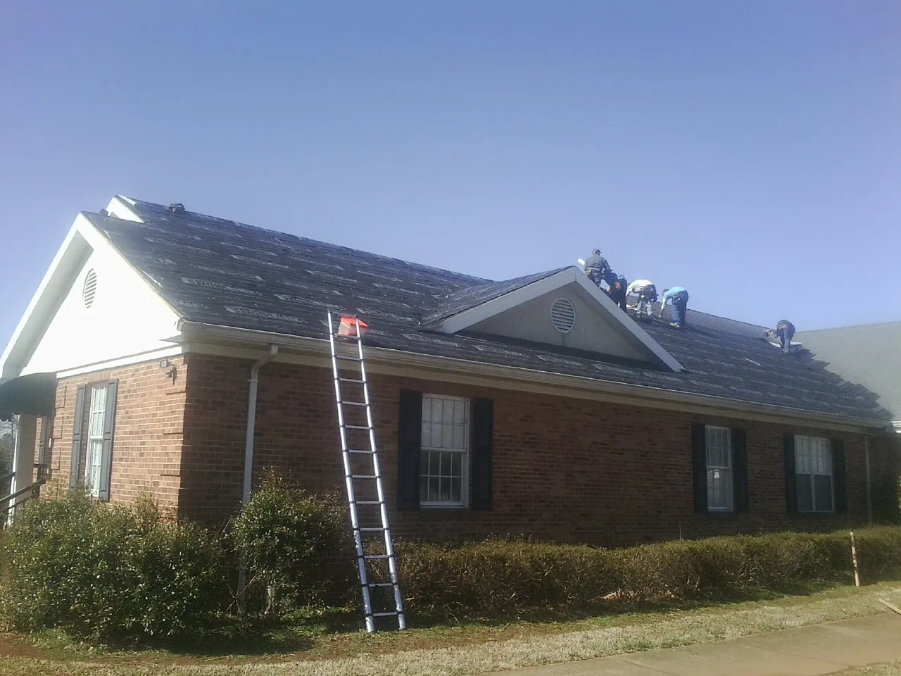 Crew tearing shingles off a brick ranch roof with a ladder set — Emergency Roof Repair work by our crew in Kennebunkport