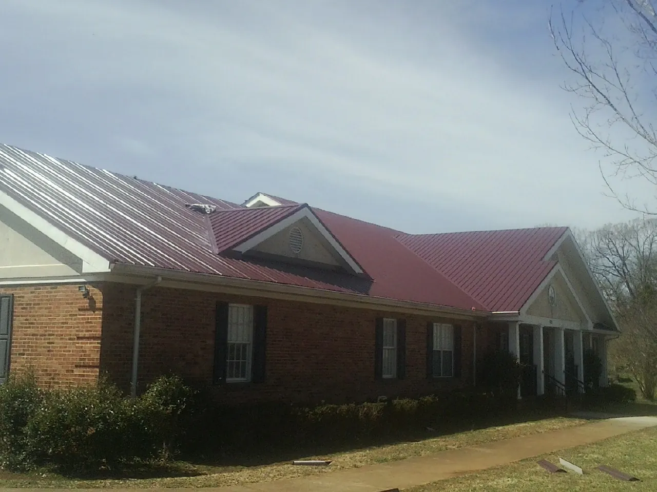 Red metal roof with gabled entries on a long brick building, from a Hail Damage Roof Repair job in Kennebunkport