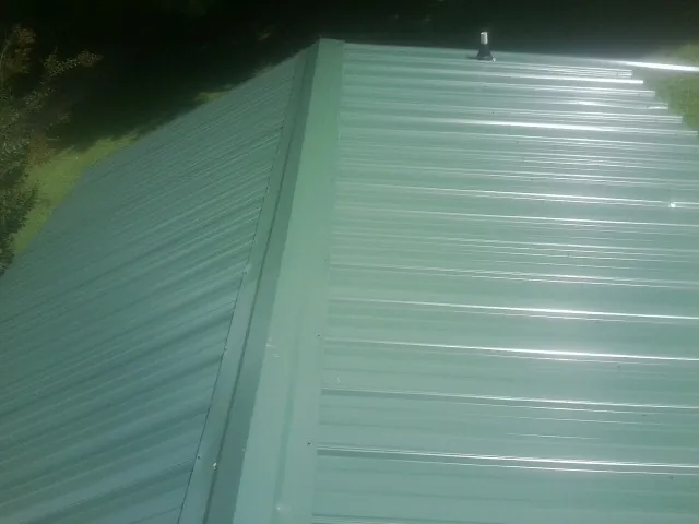 New green metal panels meeting at the ridge of a roof — Flat Roof Repair work by our crew in Kennebunkport
