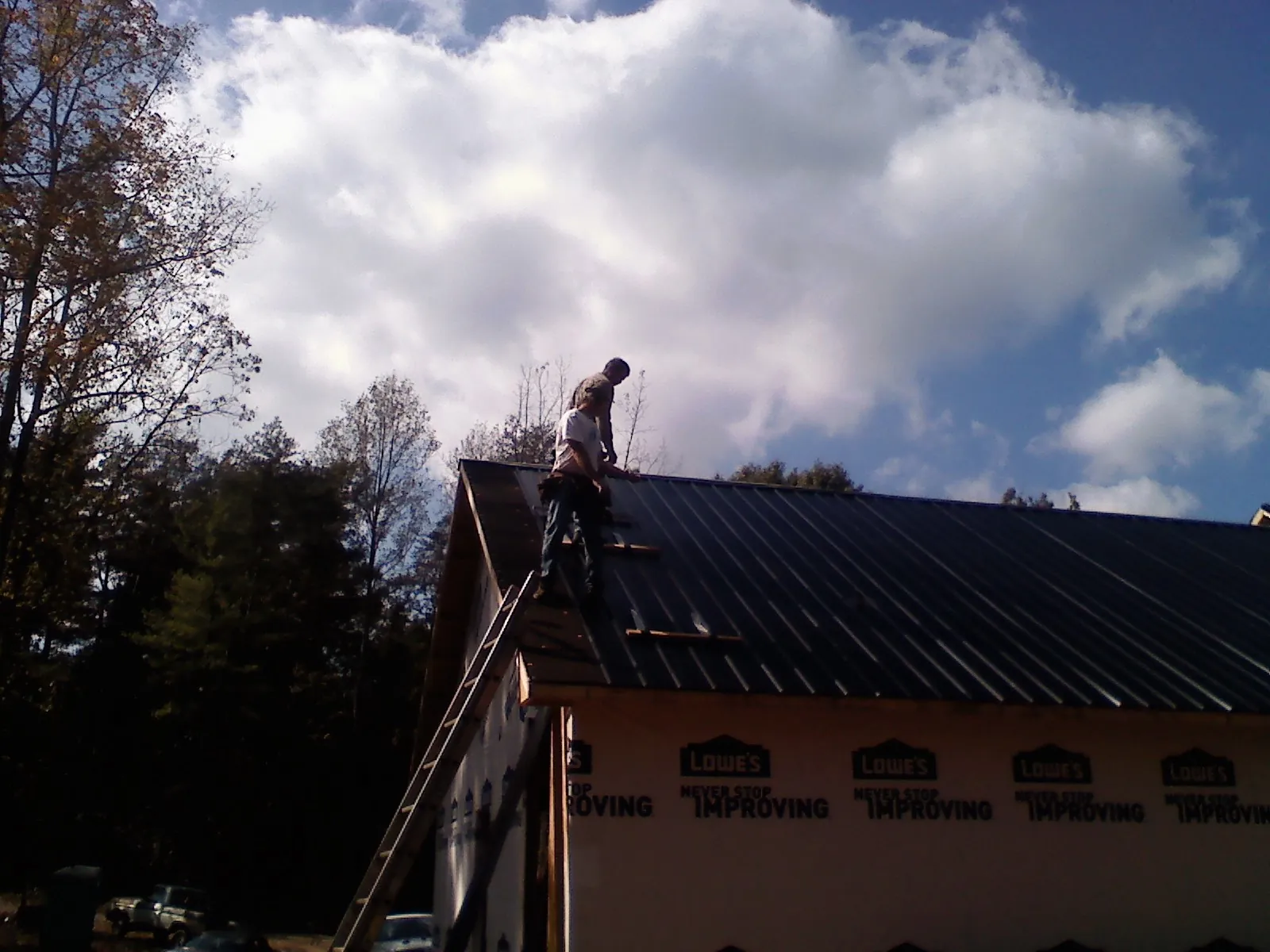 Roofer fastening dark metal panels high against a cloudy sky, from a Roof Inspection job in Kennebunkport