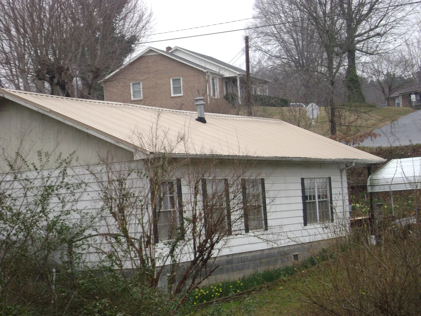 Tan metal roof on a white sided house set into a hillside — Commercial Roofing by Roofing Brothers in Kennebunkport
